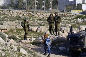 Kolme israelilaista sotilasta tien sivussa ja pieni koululainen reppu selässä.